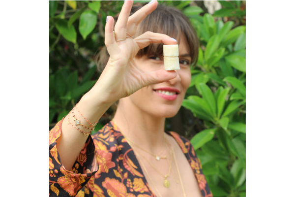 Image Smiling woman holding two natural sugar cubes in front of green foliage outdoors